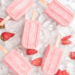 Strawberry Yogurt Popsicles sitting on ice cubes and surrounded by fresh strawberries.