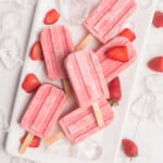 Strawberry Yogurt Popsicles on a large white plate surrounded by ice cubes and fresh strawberries.