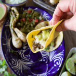 A hand holding a carne asada taco over a blue plate.