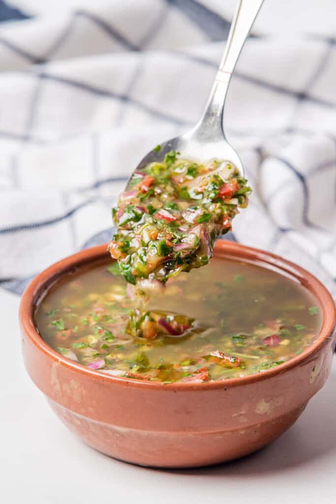 A spoonful of cilantro chimichurri over a clay bowl.