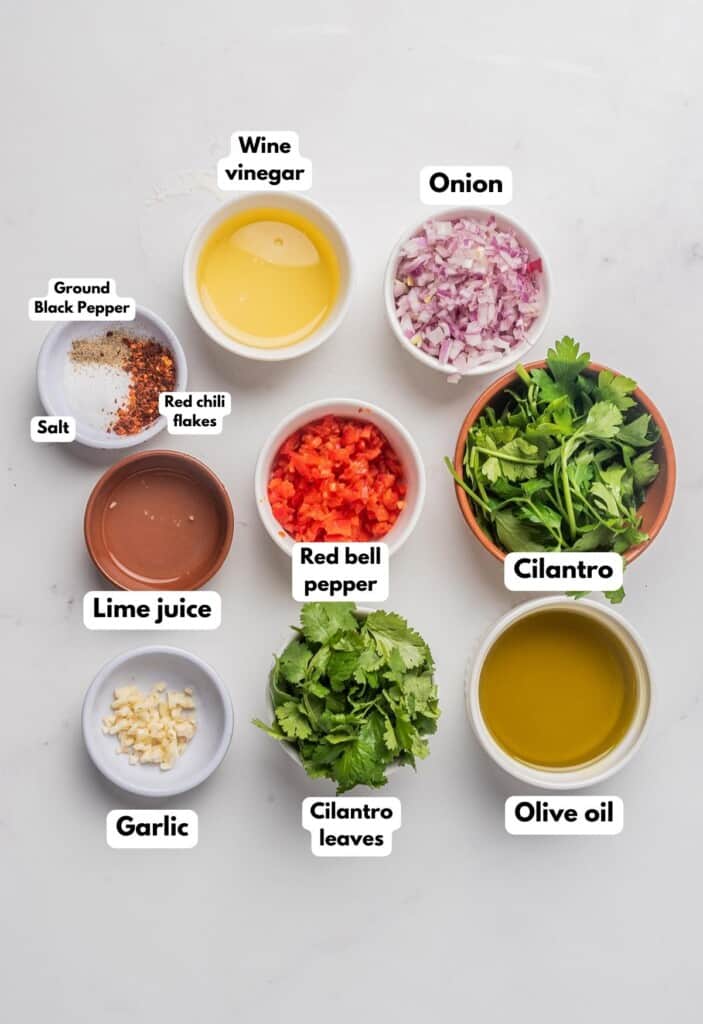 The ingredients needed to make cilantro chimichurri labeled and sitting on a marble surface.