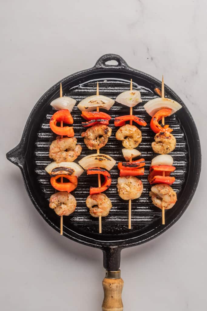 Shrimp skewers cooking in a cast iron grill skillet.
