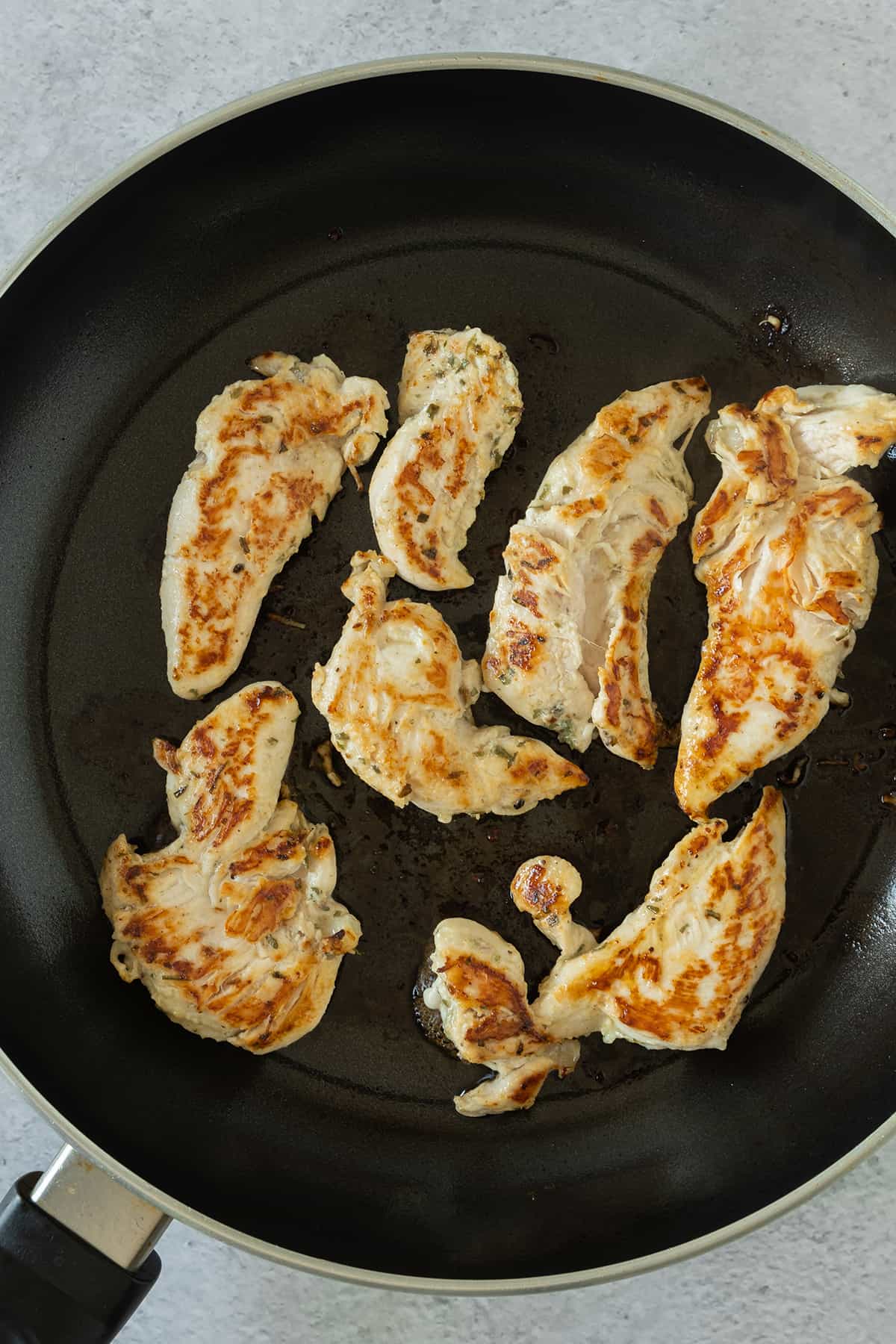 Chicken strips cooking in a black skillet.