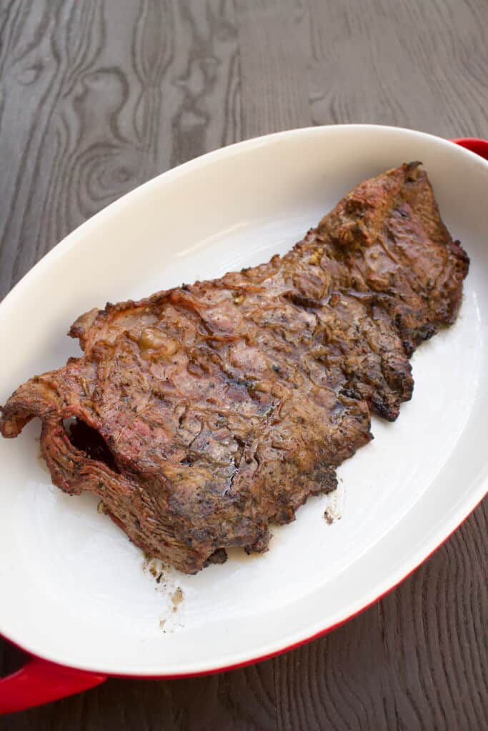 Grilled flap steak sitting on white ceramic plate.