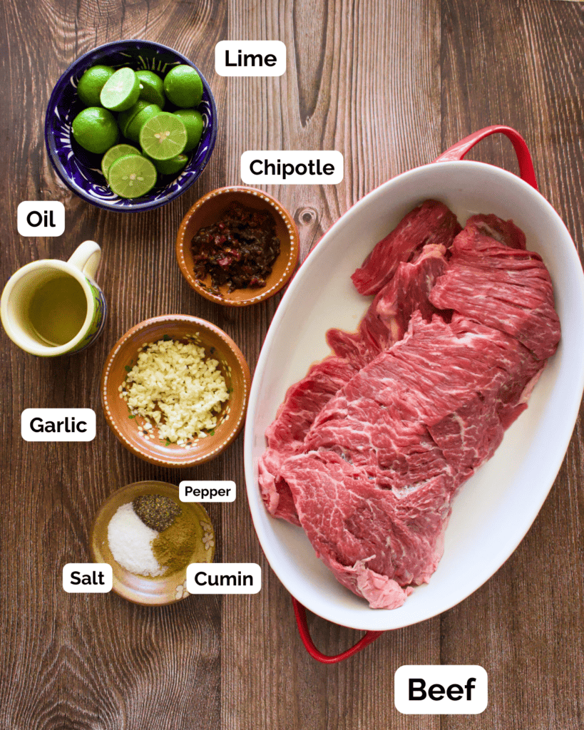 The ingredients needed to make chipotle carne asada labeled and sitting on a wooden surface.