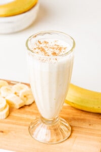 Licuado de Plátano (or Banana Smoothie) served in a glass cup next to banana slices.