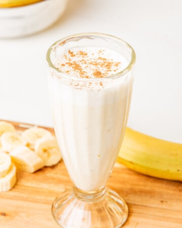 Licuado de Plátano (or Banana Smoothie) served in a glass cup next to banana slices.