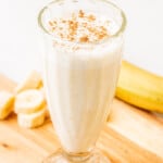 Licuado de Plátano (Banana Smoothie) served in a glass cup on a wooden cutting board.