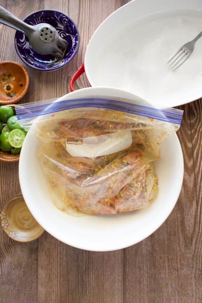 Meat marinating in a sealed plastic bag sitting inside a white bowl.