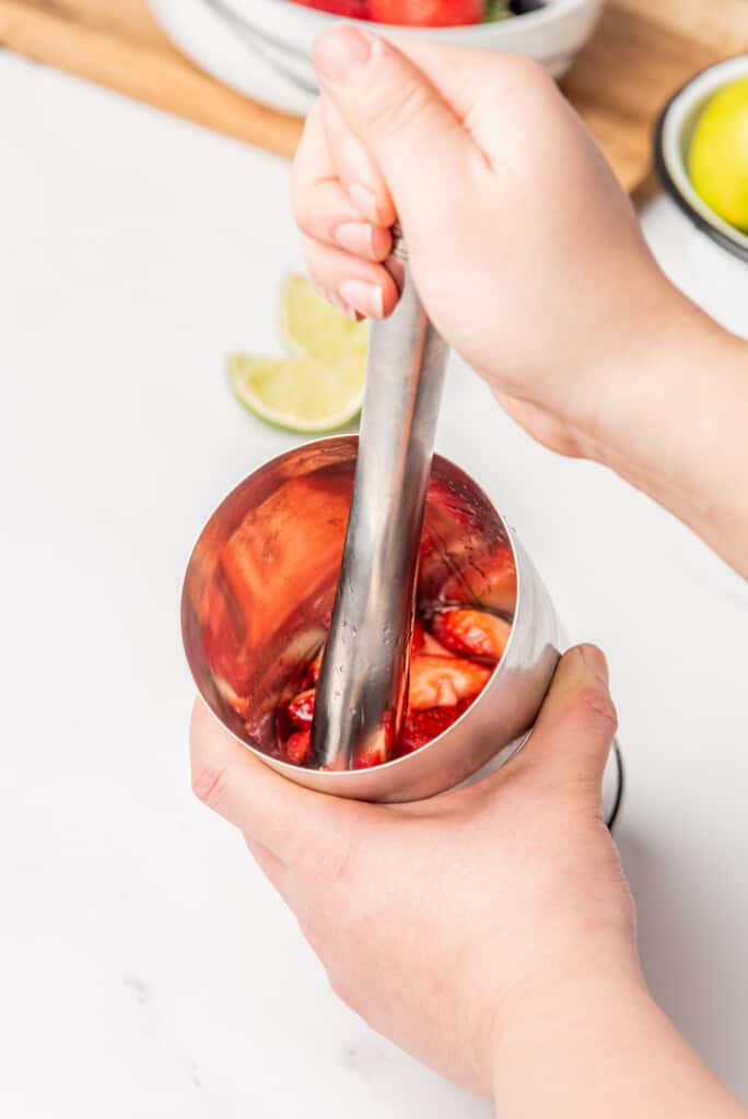 Muddling strawberry and jalapeños in a cocktail shaker.