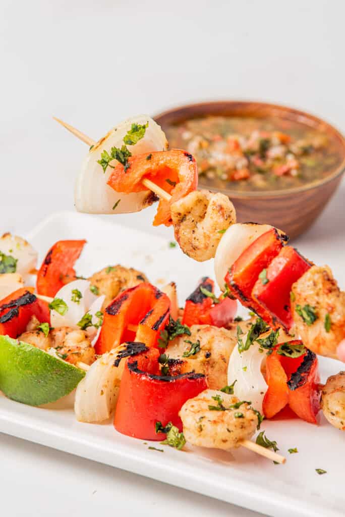 A grilled shrimp skewer over other skewers on a white plate.