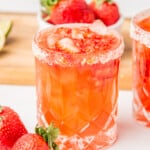 A Strawberry Jalapeno Margarita served in a glass and sitting next to fresh strawberries.