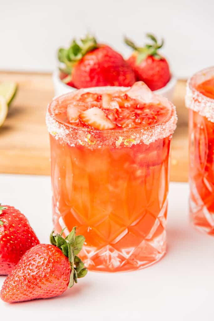 A Strawberry Jalapeno Margarita served in a glass and sitting next to fresh strawberries.