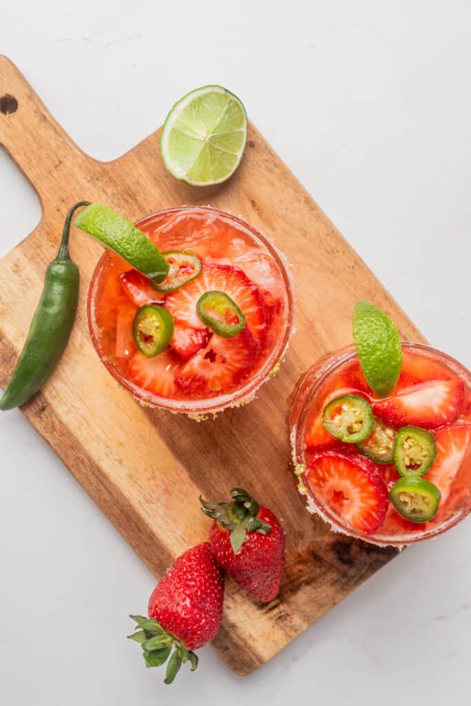 Two strawberry jalapeno margaritas topped with jalapeno slices and a lime wedge.