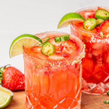 Two strawberry jalapeno margaritas topped with jalapeno slices and lime wedges.