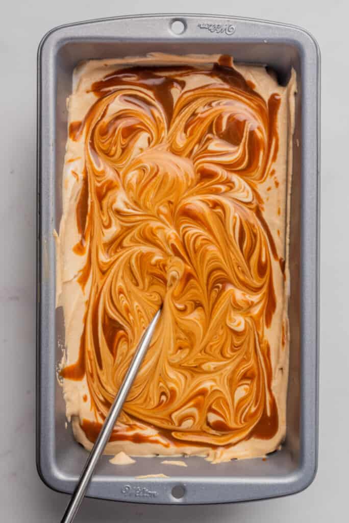 A metal stick making swirls of dulce de leche in a baking dish.