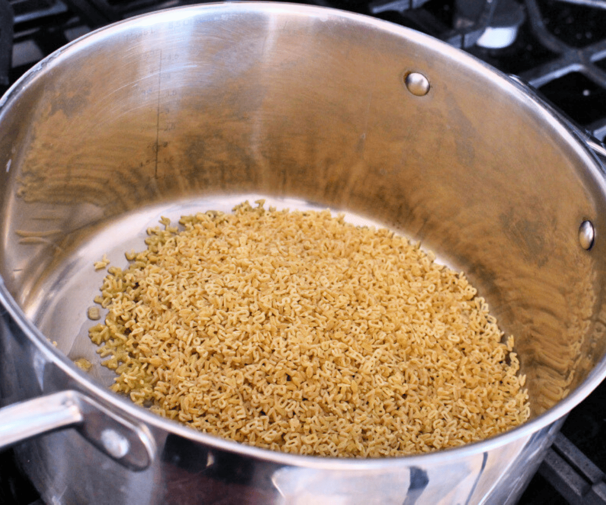 Alphabet pasta toasting inside a metal stockpot.