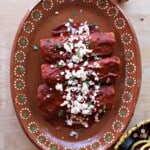 Enchiladas Rojas served on a decorative clay plate and topped with cheese and cilantro.