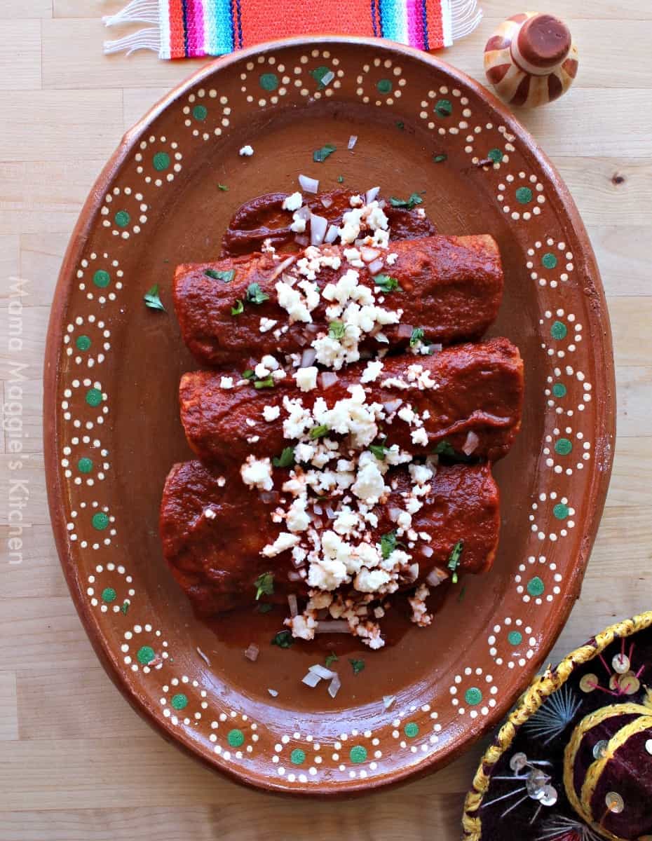 Enchiladas Rojas served on a decorative clay plate and topped with cheese and cilantro.