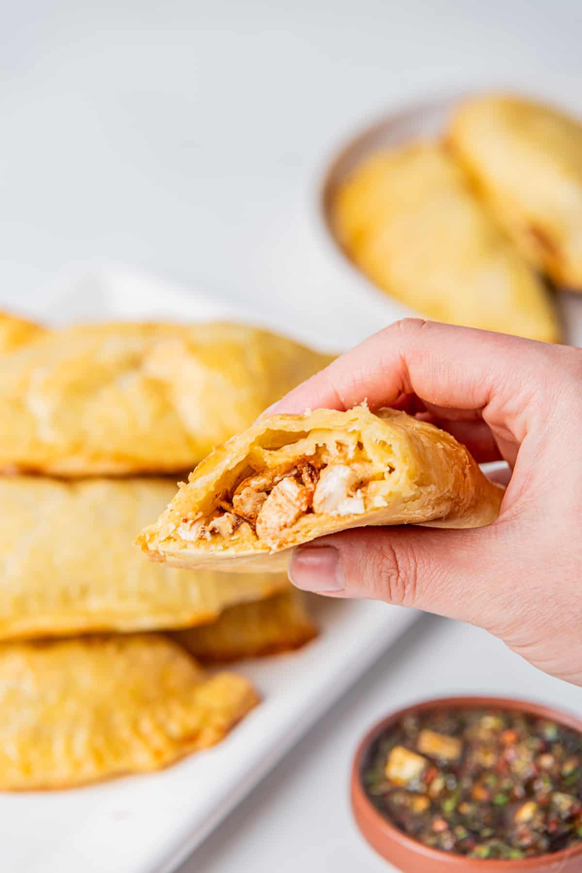 A hand holding half of Empanada de Pollo and showing the filling.