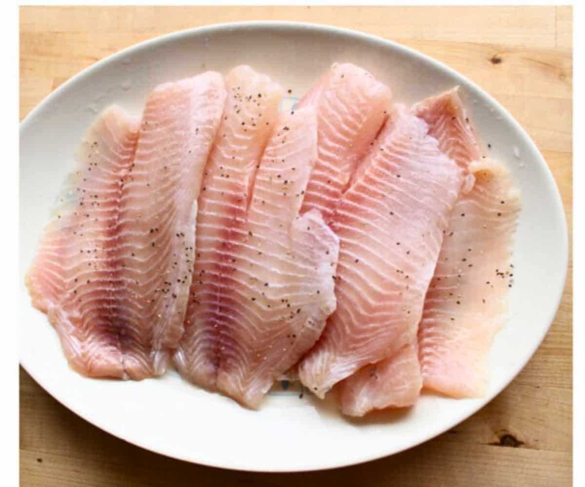 Raw white fish seasoned and sitting on a white plate.