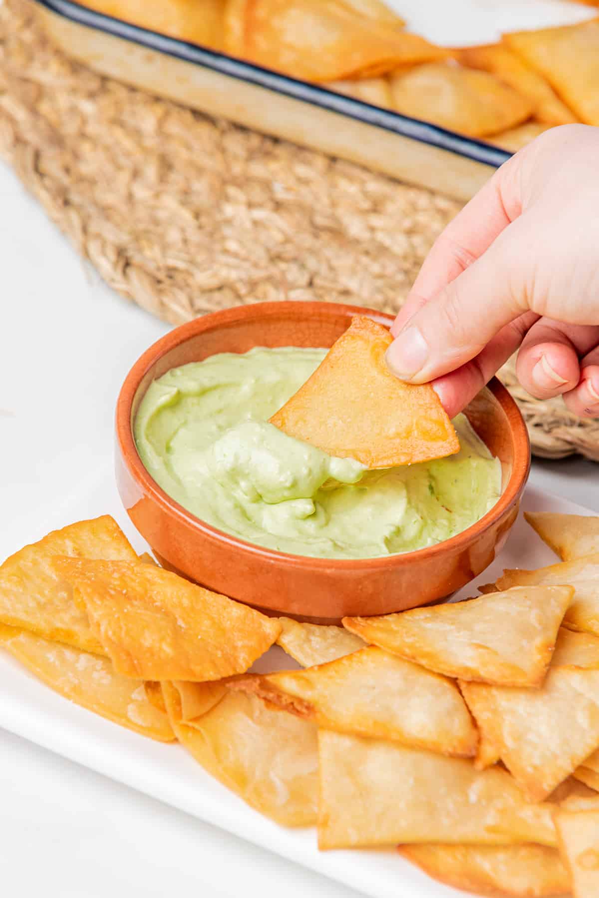A hand dipping a chip into creamy guacamole.