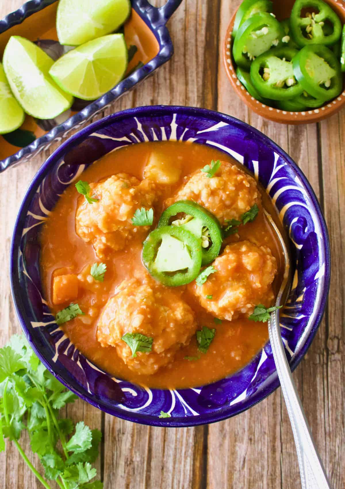 Albondigas de Pollo (or Chicken Meatball Soup) served in a decorative Mexican blue plate and topped with cilantro and sliced jalapeno.