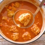 A ladle holding a meatball over a stock pot.