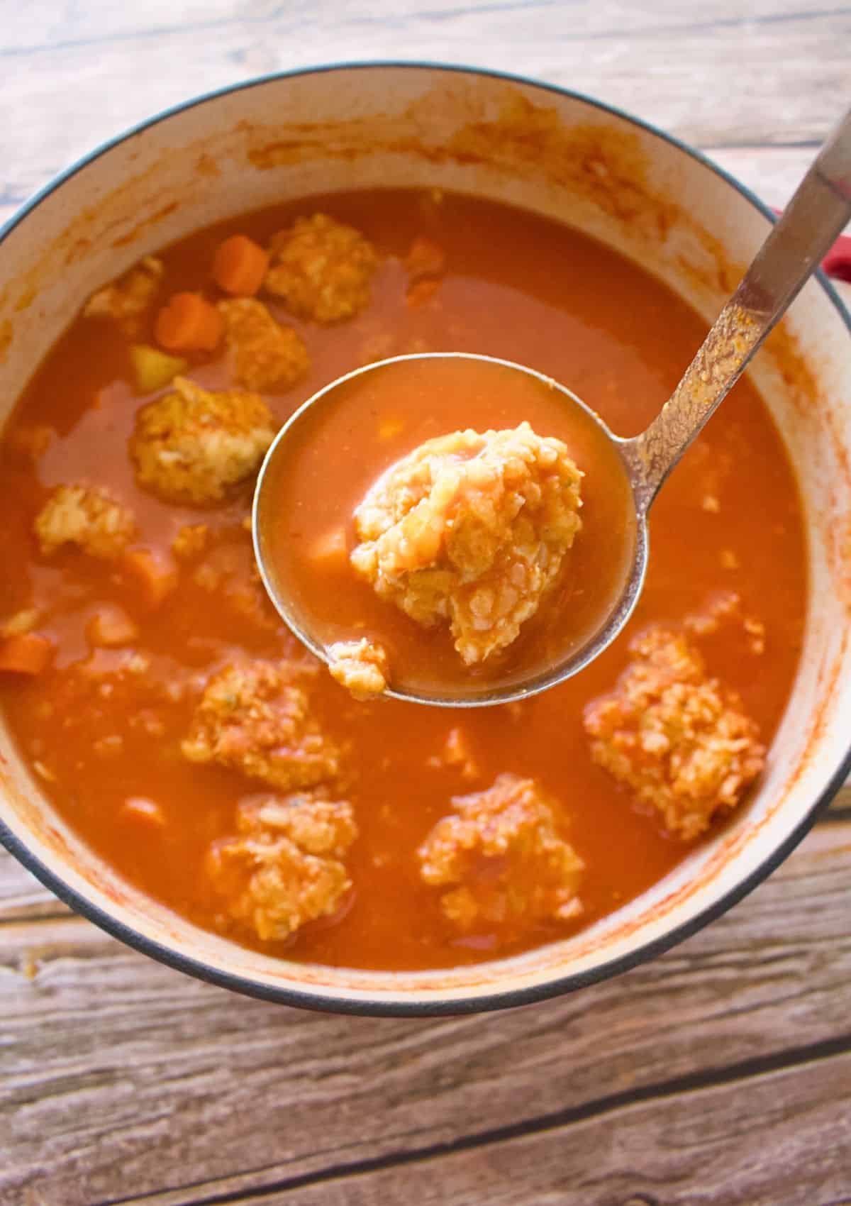 A ladle holding a meatball over a stock pot.