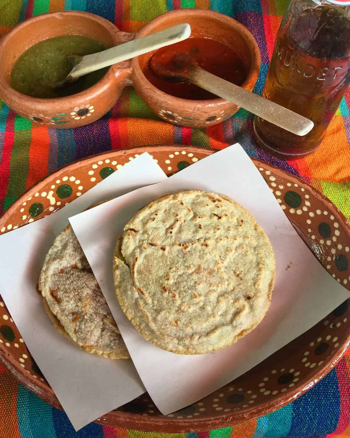 Two Mexican Gorditas plated on a decorative red clay plate.