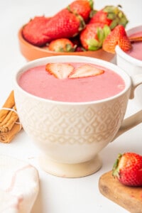 A cup of atole de fresa served in a white ceramic mug and surrounded by fresh strawberries.