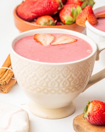 A cup of atole de fresa served in a white ceramic mug and surrounded by fresh strawberries.