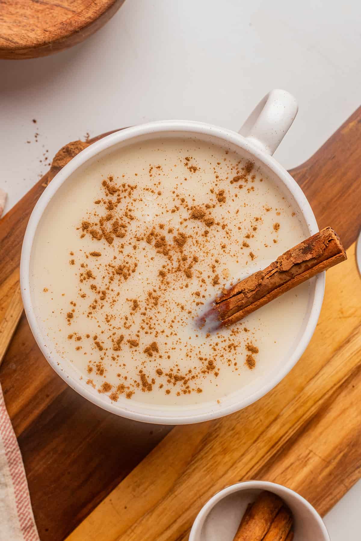 Atole de Vainilla served in a mug topped with ground cinnamon and a whole cinnamon stick.