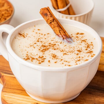 Atole de Vainilla served in a white mug topped with ground cinnamon and a whole cinnamon stick.