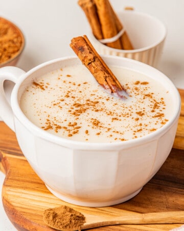 Atole de Vainilla served in a white mug topped with ground cinnamon and a whole cinnamon stick.