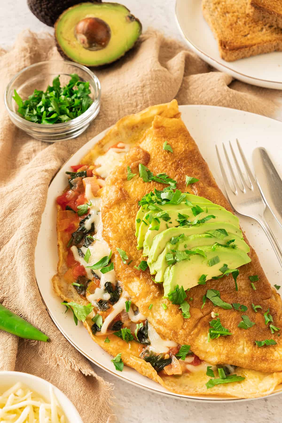 A California Omelette served on a white plate and topped with avocado slices and chopped cilantro.