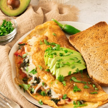 A California Omelette topped with avocado slices and chopped cilantro and served next to toast.