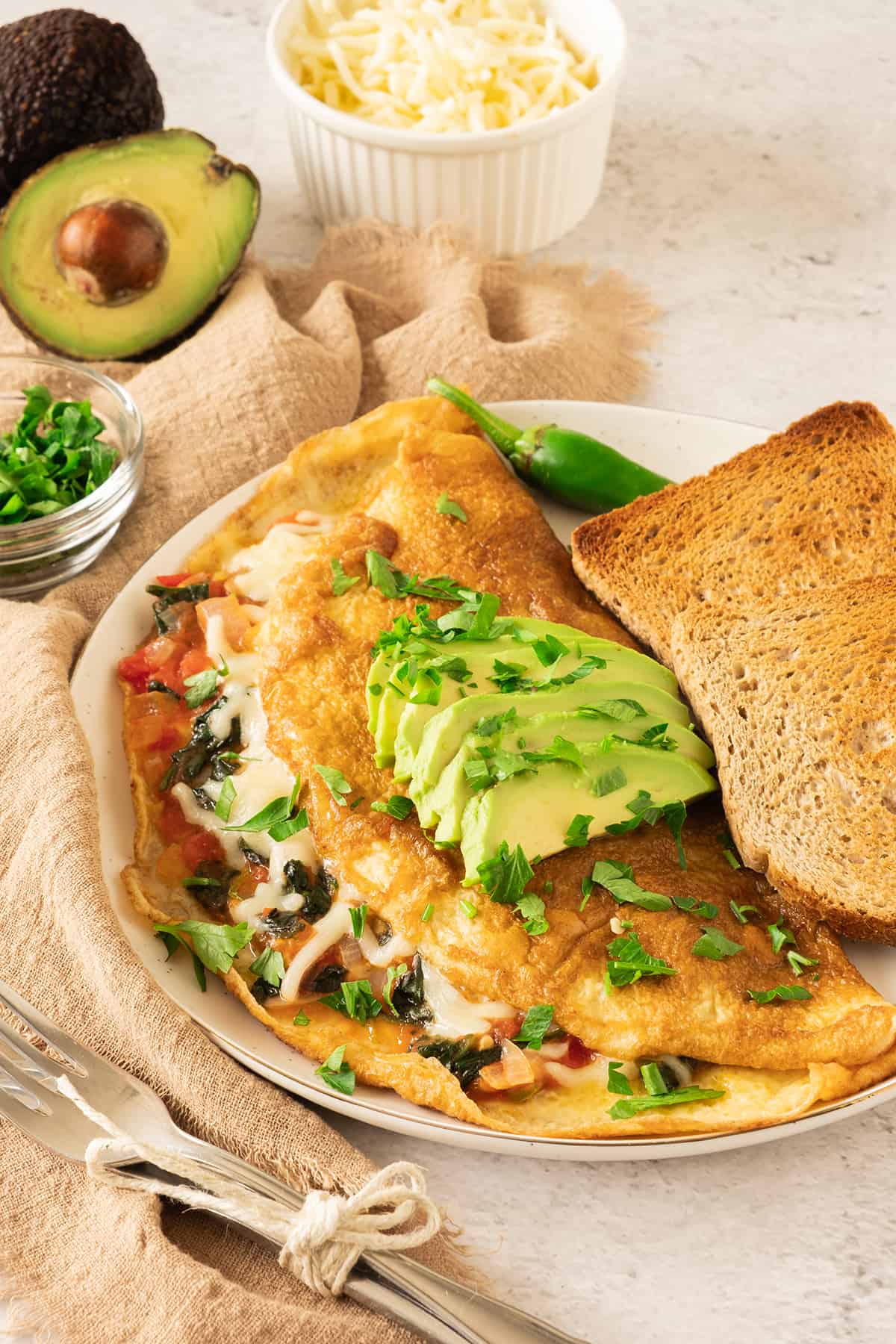 A California Omelette topped with avocado slices and chopped cilantro and served next to toast.