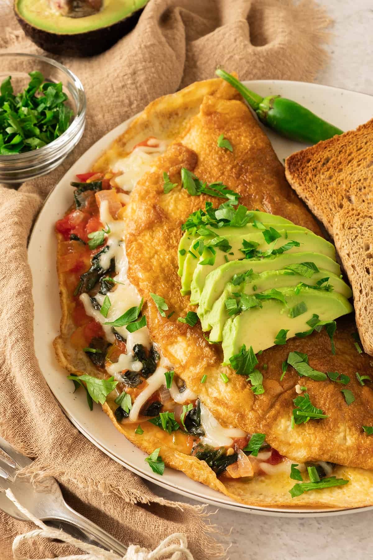 A California Omelette served on a white plate and topped with avocado slices and chopped cilantro.