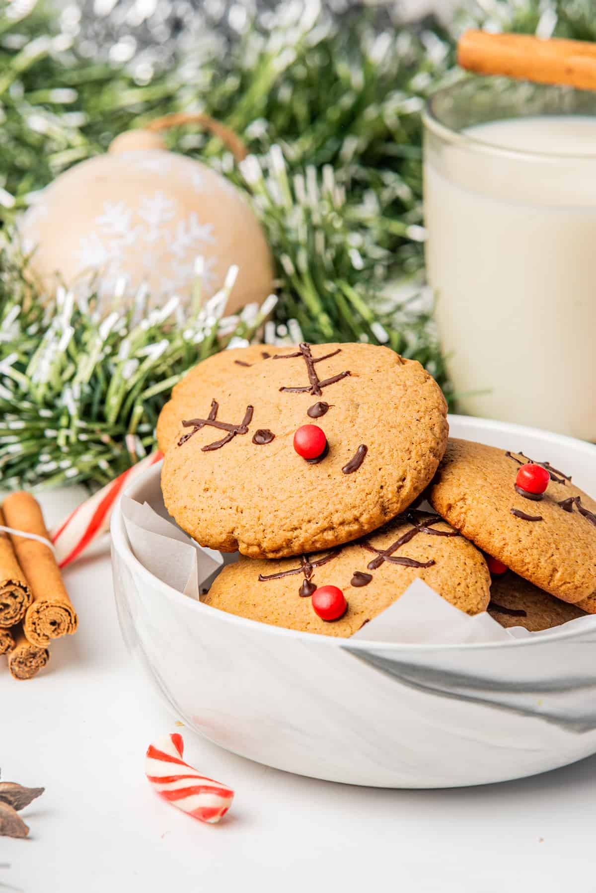 Gingerbread Reindeer Cookies in a white bowl next to Christmas decorations.
