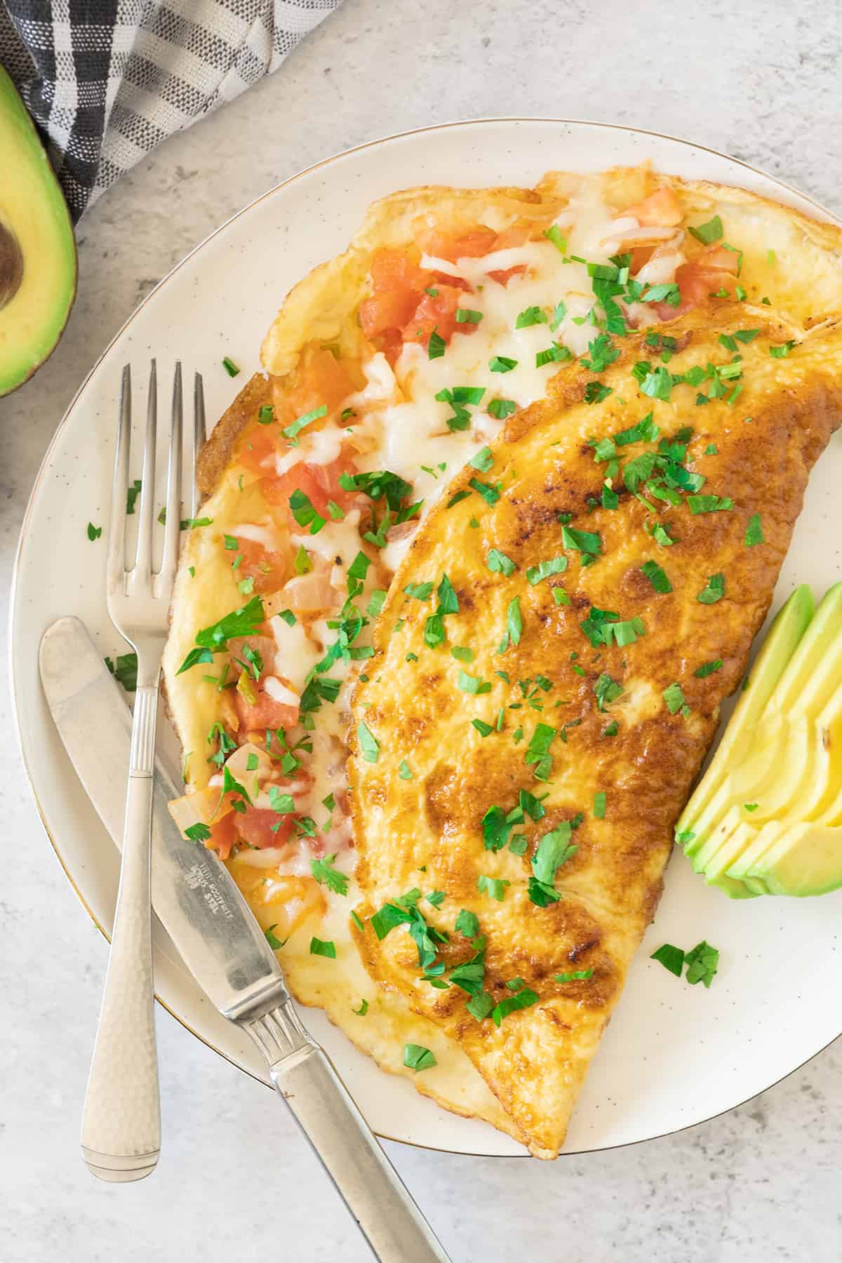 A Mexican Omelette served on a white plate next to avocado slices.