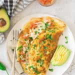 A Mexican Omelette served on a white plate next to avocado slices.