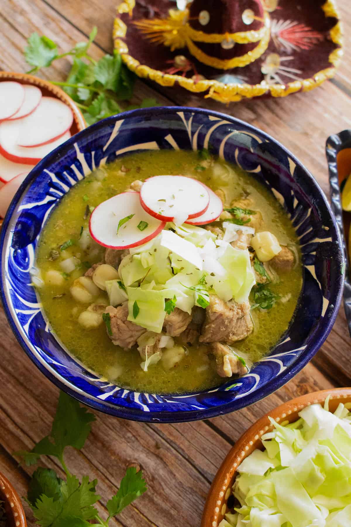 Pork Pozole Verde served in a blue bowl and topped with cabbage, radishes, and cilantro.