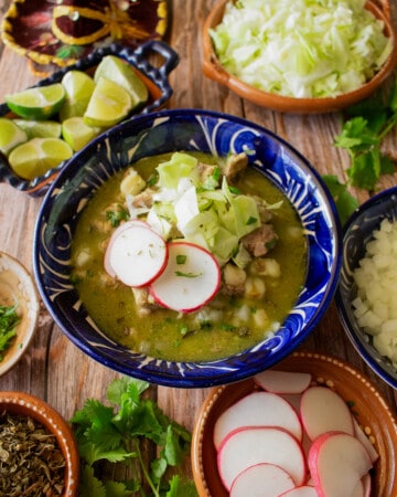 Pork Pozole Verde served in a blue bowl and topped with cabbage, radishes, and cilantro.