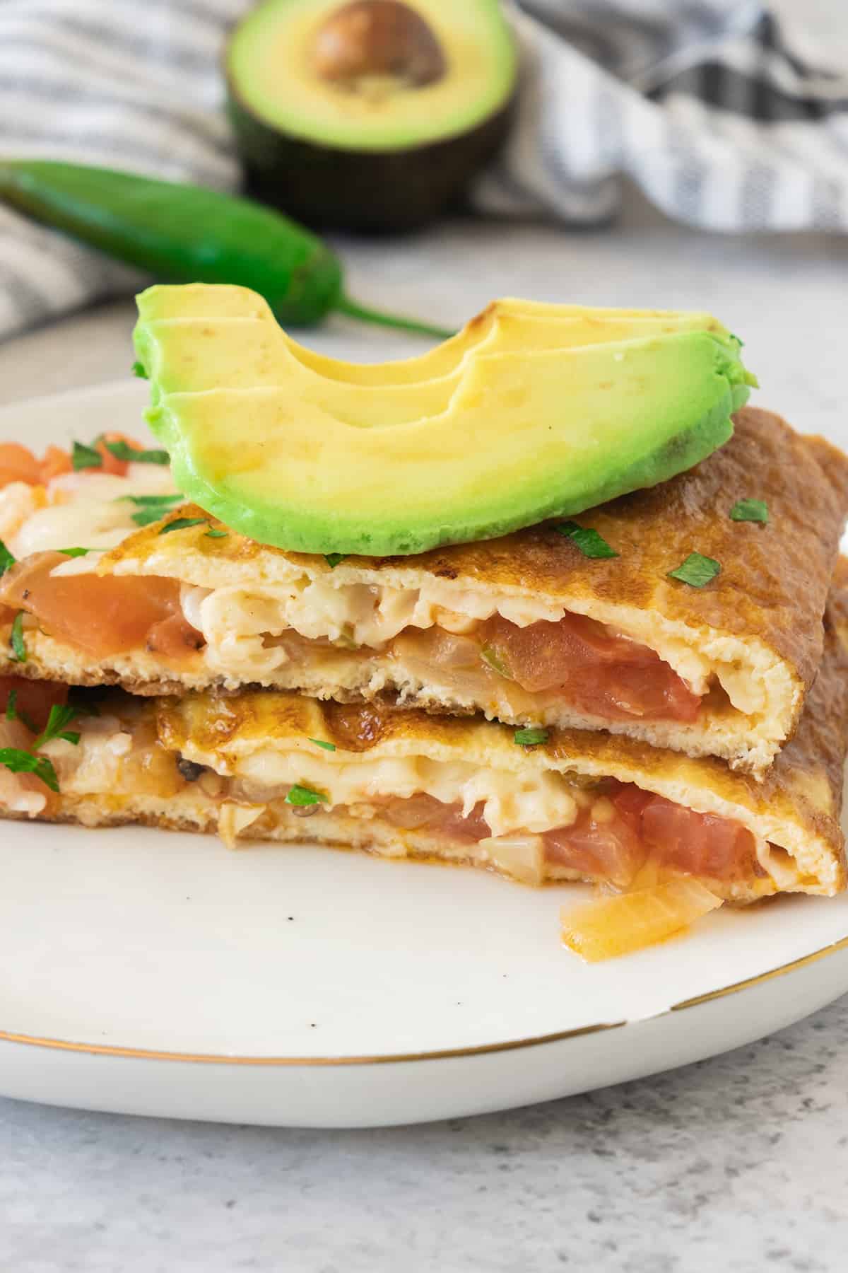 A Mexican omelette cut in half and topped with avocado slices.
