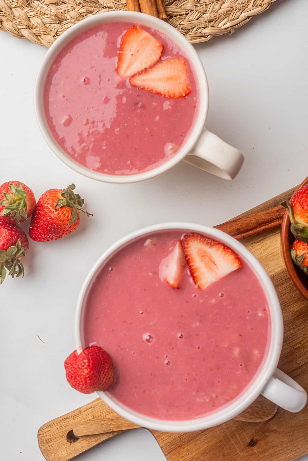 Two mugs with Atole de Fresa topped with fresh strawberry slices.