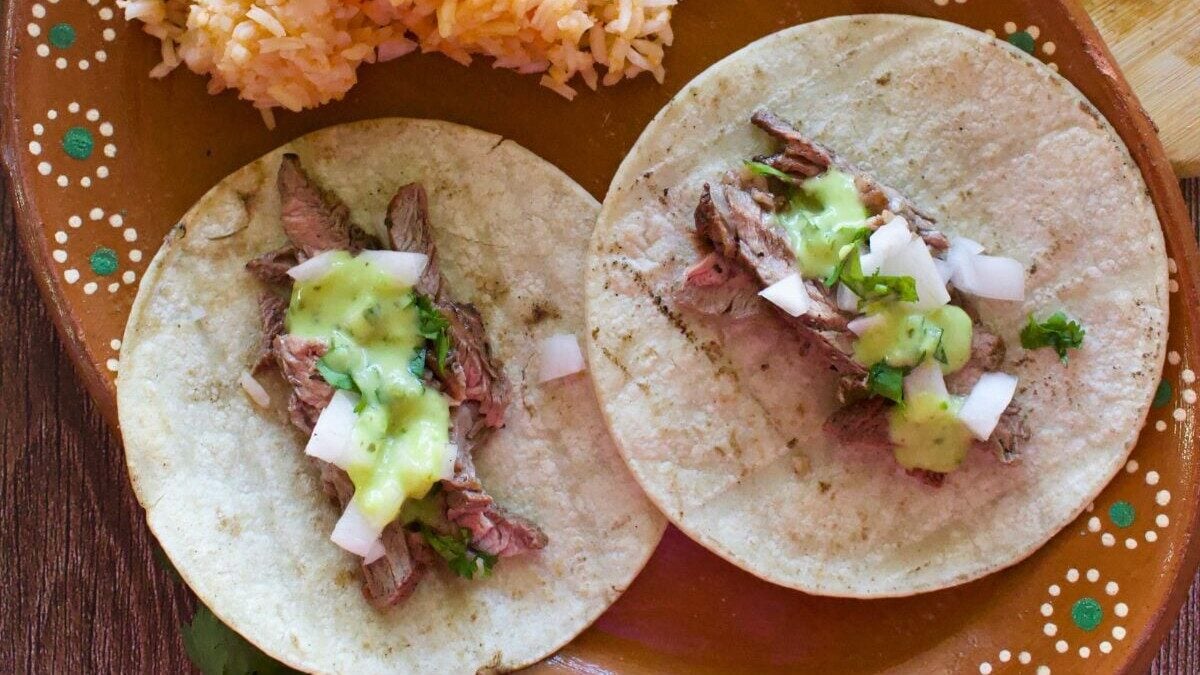 Chipotle carne asada tacos served on a decorative Mexican plate next to red rice.