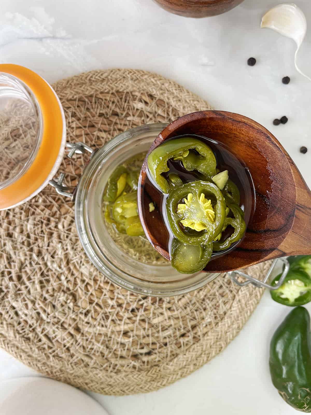 A wooden spoon removing pickled jalapenos from a glass jar.
