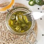 A fork removing pickled jalapenos from a jar.