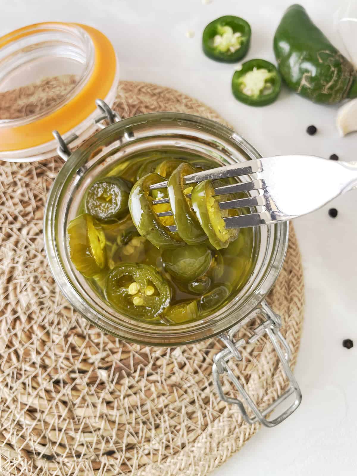 A fork removing pickled jalapenos from a jar.